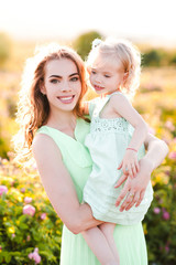 Smiling woman holding baby girl 3-4 year old over sunny nature background. Looking at camera. Motherhood.