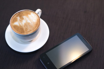 A cup of coffee, a smartphone in a cafe with a blurred background.
