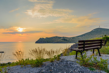 Fototapeta na wymiar Beautiful sunset on the sea. Viewpoint with a bench on top of a hill. Skala village on Patmos island, Dodecanese, Greece.