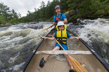 Young boy paddling whitewater in a canoe