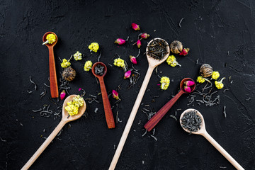 Aromatic tea. Wooden spoons with dried tea leaves, flowers and spices on black background top view