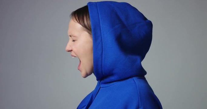 Young woman in large unlabeled bright blue hoodie screams and acts scared and angry isolated on white