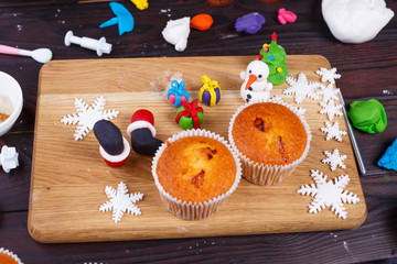 Ready to decorating sweet tasty homemade cupcakes and Christmas decorations made of confectionery mastic on the board. Family culinary and New Year traditions concept, festive food, party treats