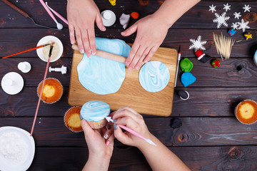 Friends rolling confectionery mastic and decorating cupcakes, view from above. Family culinary and New Year traditions concept, festive food, party treats, togetherness, cooking process