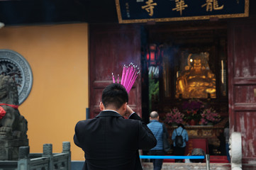 Chinese man is praying at a Buddhist temple and burning incense sticks