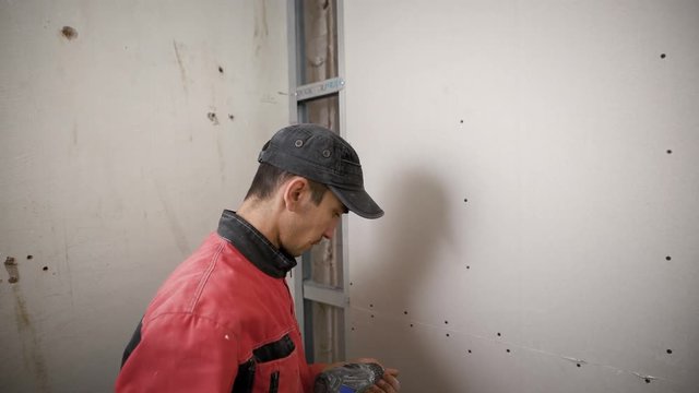 Builder in uniform installing panels on wall using electric drill