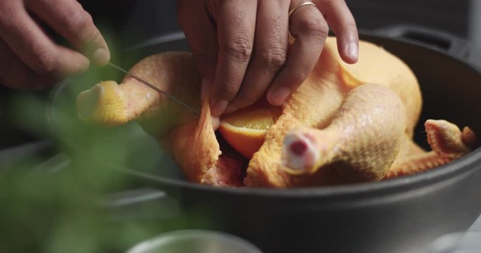 Dark skinned male cook prepares a large chicken for roasting with orange and rosemary