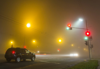 Thick fog over empty road with lonely car and traffic lights at night
