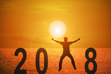 Silhouette of young man jumping on the beach between 2018 years with beautiful sunset at the sea, concepts of news year and business target.