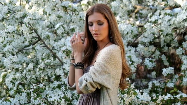 Beautiful young woman in long dress boho style under apple tree in blossom in garden
