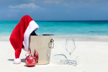 Champagner mit Weihnachtsmütze und Gläsern am tropischen Strand mit türkisem Wasser