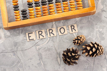 Word ERROR laid out of handwritten letters on cardboard squares near old wooden abacus and three cones on gray cracked concrete