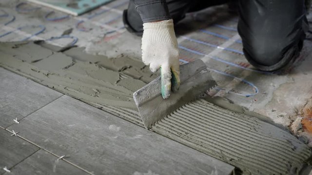 Anonymous site worker applying cement on floor and laying tiles