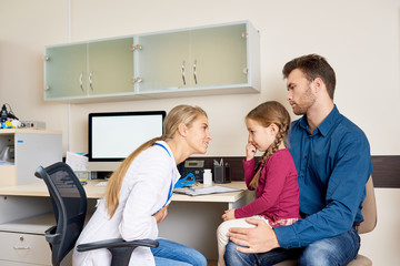 Side view portrait of female pediatrician talking to cute little girl visiting doctor for consultation with her father