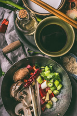 Wok with chopped vegetables and spices on kitchen table background with chopsticks,  soy sauce and sesame oil. Asian food , Chinese or Thai cuisine concept