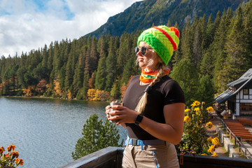 Happy young woman standing on a terrace with a cup in her hands and looking on lake