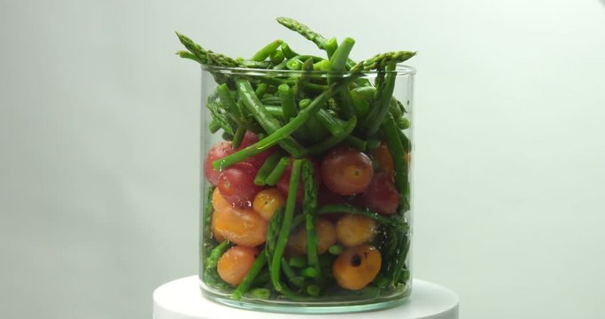 Steamed multicolor cherry tomatoes, asparagus and green beans (haricots verts) in a round tall vase ready for festive table on white background