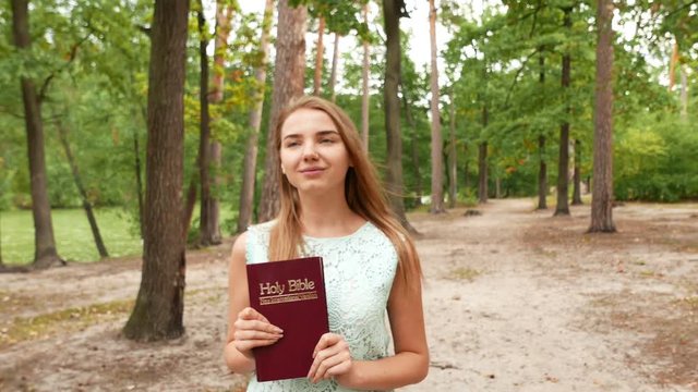 4k. Attractive girl  with Bible in park. Christian team  steady shot