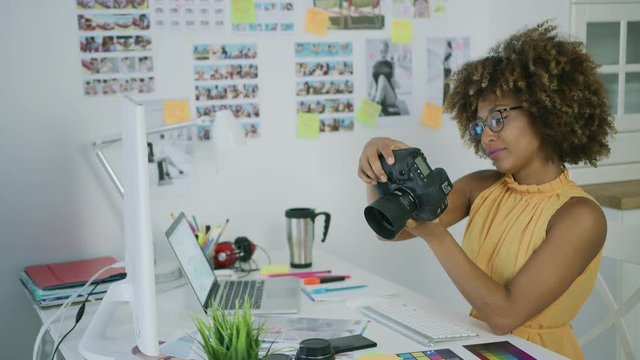 Elegant young woman in glasses working as creative designer in office and watching photos on camera sitting at table.