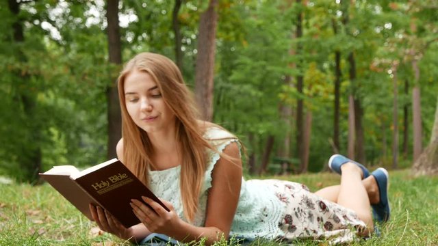 4k. Laying slender girl  read Bible in park. 