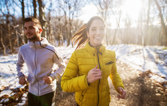 Positive beautiful young healthy couple running with sportswear through the forest in the sunny winter morning.