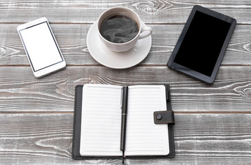 On a wooden table there is a cup of coffee, a cell phone, an address book, a pen, money