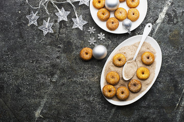 Appetizing ruddy traditional donuts with sugar and cinnamon on an oval dish on a gray grunge trendy background with a Christmas graceful neat decor with silver stars and a garland. Top View.