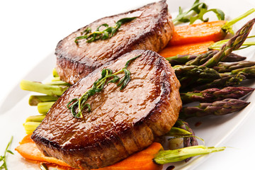 Grilled beef steaks with asparagus and carrots on white background 