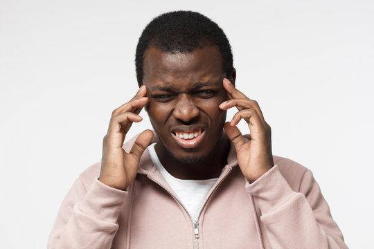 Studio picture of handsome African guy pictured isolated on white background in casual clothes suffering from severe headache trying to cope with it and concentrate on problem or task touching temples