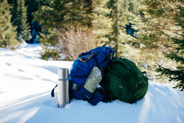 Two sports backpacks, a thermos, a map on the background of a winter mountain forest