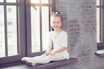Little cute child girl in white dance form sitting on window at modern dance studio