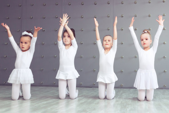Group of four little ballerinas and kid ballerun posing together and practicing for their first performance in different dance poses