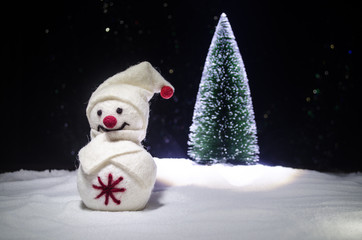 New Year. The snowman unloads gifts for the new year. White snowman surrounded by Christmas trees on evening background. Toy Decoration