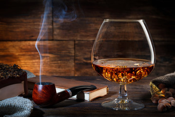 Glass of whiskey with ice, notebook and smoking pipe on a old wooden table