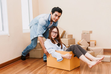 Happy couple having fun and moving woman sitting in a cardboard box at home