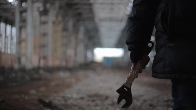 Close up video of maniac or stalker or killer man hand with dirty wrench tool in hand as weapon on background of abandoned warehouse, apocalipce horror concept