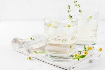 Summer refreshing drinks, infused herbal water, iced tea. Chamomile Honey and Whiskey Cocktail with thyme in glasses, on a white marble table. Copy space
