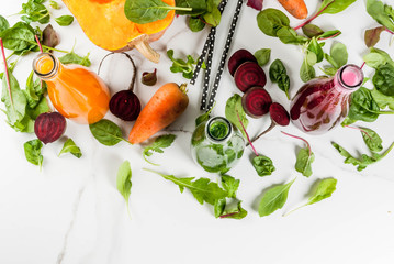 Vegan diet food. Selection colorful fresh organic smoothies drinks with autumn vegetables: beetroot, pumpkin, carrot, leafy vegetables. In bottles, white table. Copy space top view