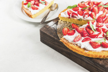 Homemade biscuit cake with whipped cream, fresh organic raw strawberries and mint. On a white stone table. Copy space