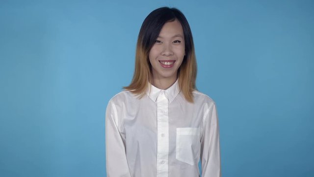 young asian woman posing showing hand gesture like on blue background in studio. attractive millennial girl wearing white casual shirt looking at the camera smiling