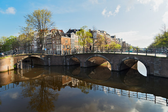 Houses and arches of bridge over canal with mirror reflections, Amsterdam, Netherlands