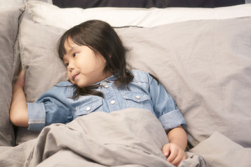 Asian children cute or kid girl sleeping or sleepy and open eye on gray bed and bedtime for relax in bedroom at home on warm white with space