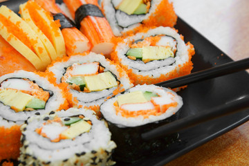 delicious sushi roll seaweed with salmon raw shrimp eggs and sesame on black dish and wood table with chopsticks for lunch or dinner at japanese food restaurant with space