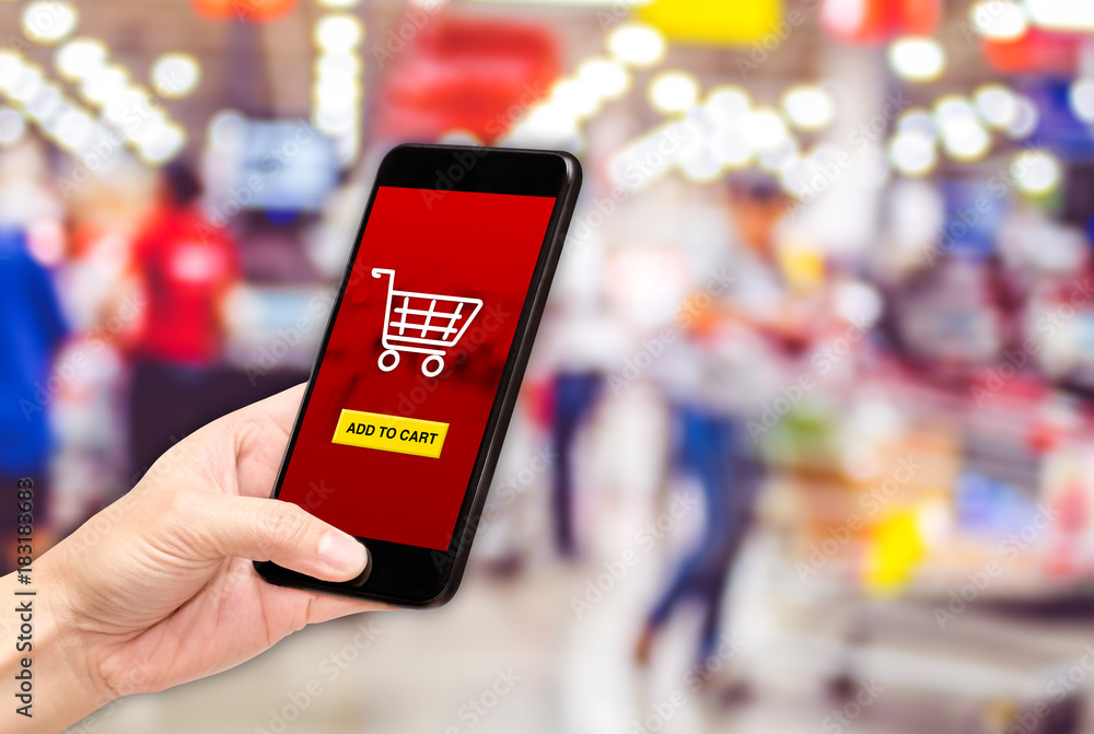 Poster Hand holding mobile add to cart product to purchase online with apps screen at blur bokeh supermarket background,online shopping concept,digital lifestyle.