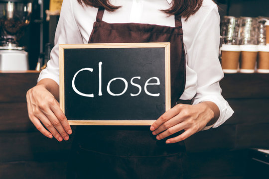 Barista holding chalkboard with word CLOSE in coffee shop restaurant