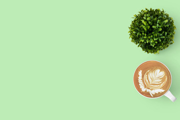 Green pastel office table of a hipster with latte coffee and a small rounded tree. Top view with copy space, flat lay.