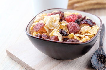 cornflakes and dry berry fruits in a brown bowl on a wooden background.
