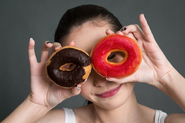 Woman holding calorie bomb donut on gray background. Junk food concept