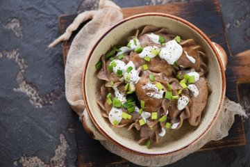Top view of rye vareniki or dumplings with sauerkraut served in a bowl over dark brown stone background, horizontal shot