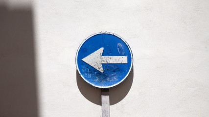 Blue direction arrow sign next to wall